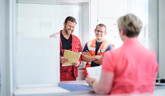 Ein Fahrer, ein Mitarbeiter vom Hof und eine Mitarbeiterin aus dem Büro unterhalten sich gut gelaunt.
